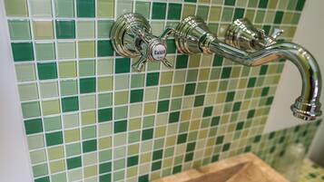 Un baño con pared de mosaicos verdes y grifo de cromo.