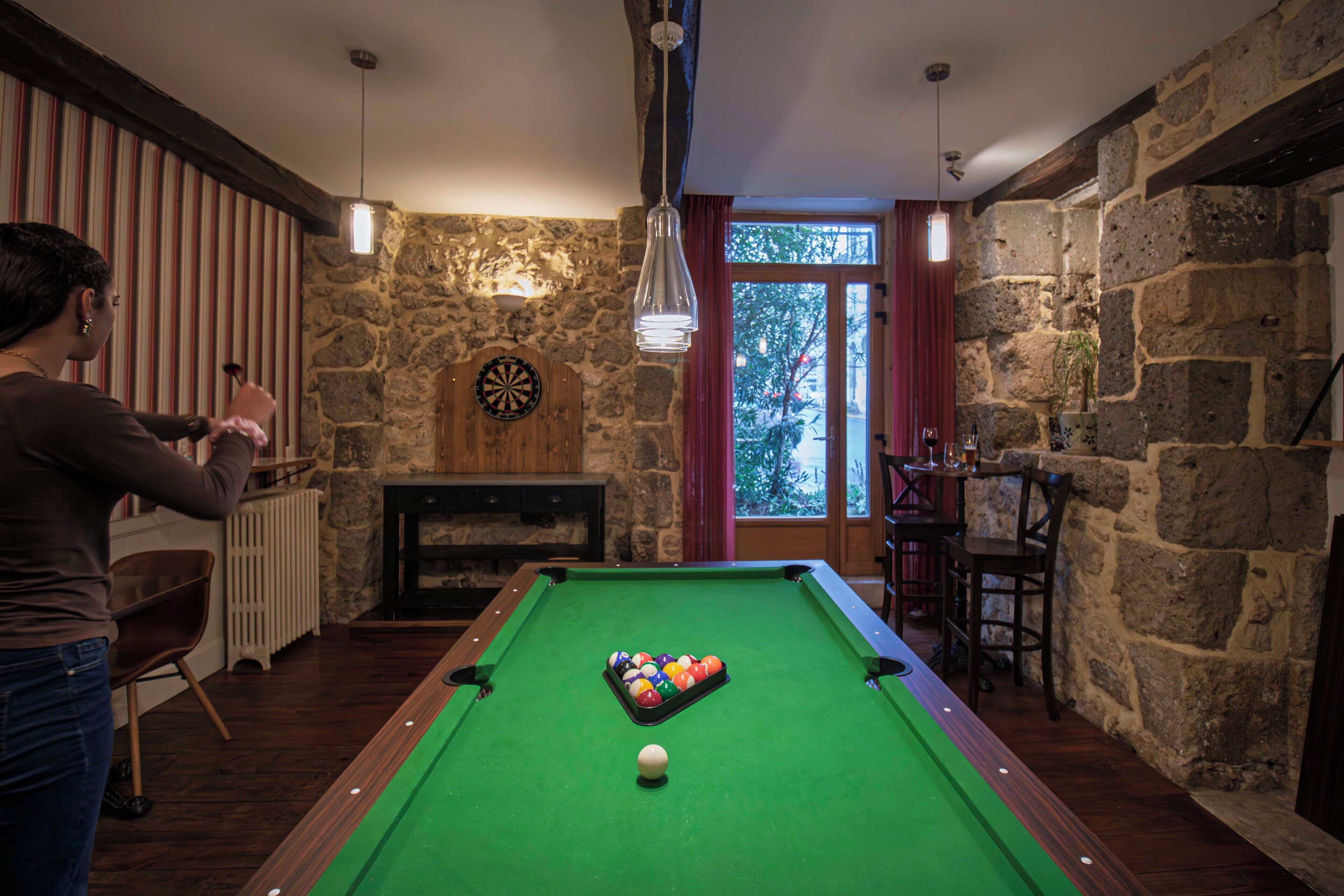 A pool table in a room with stone walls, a dartboard, and a window with a view of trees.