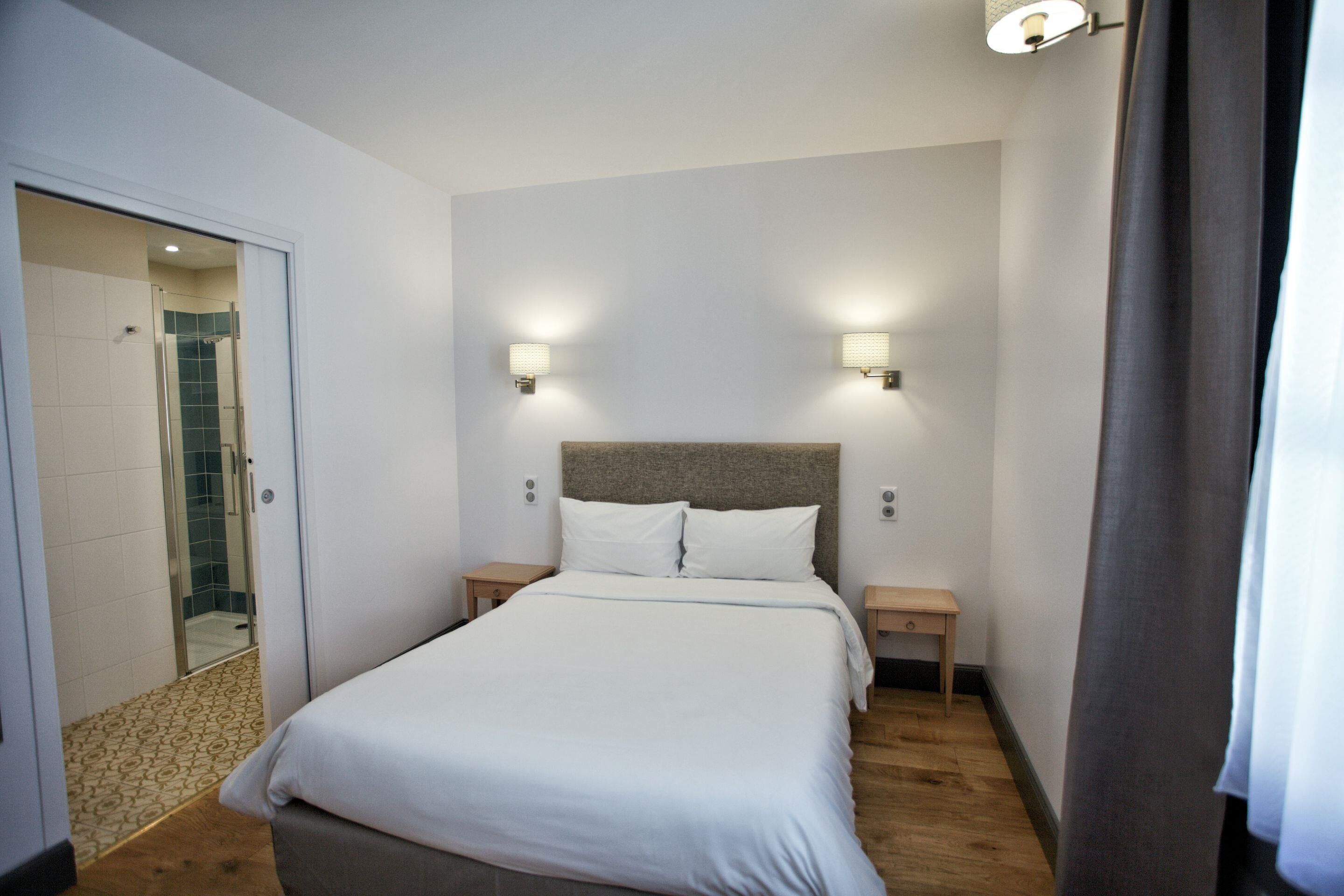 A hotel room with a bed, two bedside tables, a headboard, and a shower area.