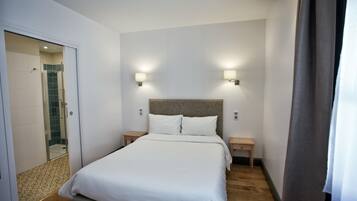 A hotel room with a bed, two bedside tables, a headboard, and a shower area.