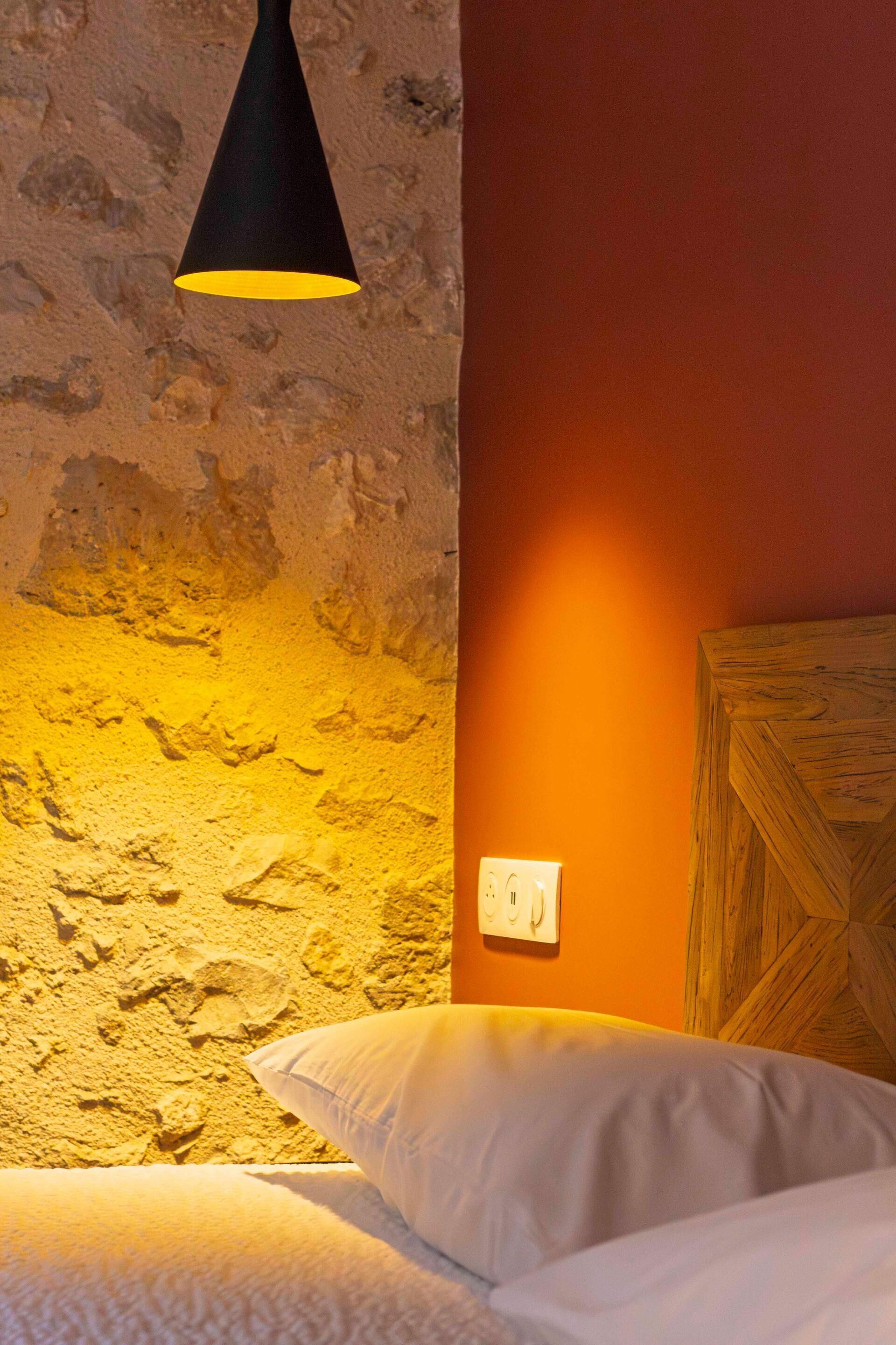 A bedroom with a stone wall, a wooden headboard, and a black pendant light.