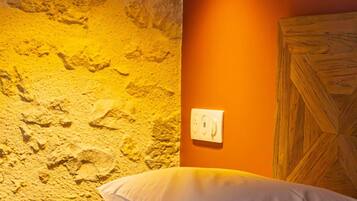 A bedroom with a stone wall, a wooden headboard, and a black pendant light.