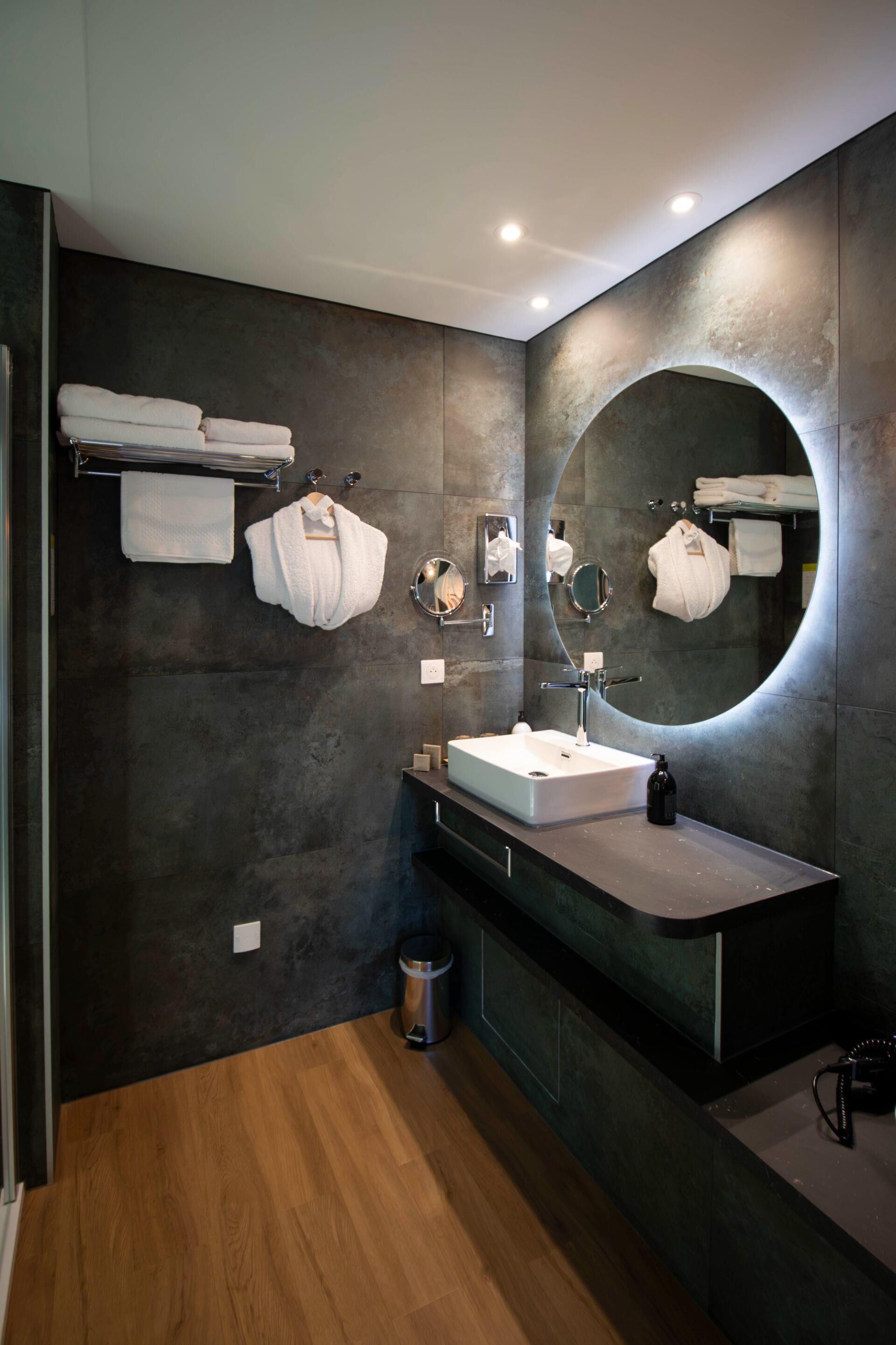 A modern bathroom with a large mirror, a rectangular sink, and multiple towels on a rack.