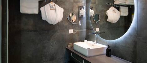 A modern bathroom with a large mirror, a rectangular sink, and multiple towels on a rack.