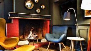 Una habitación acogedora con chimenea, dos sillones, una mesita y una lámpara.