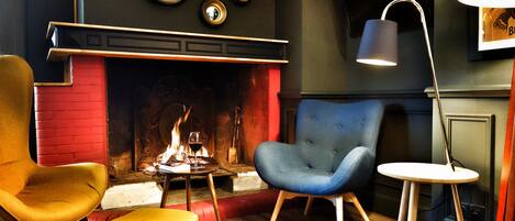 A cozy room with a fireplace, two armchairs, a small table, and a lamp.
