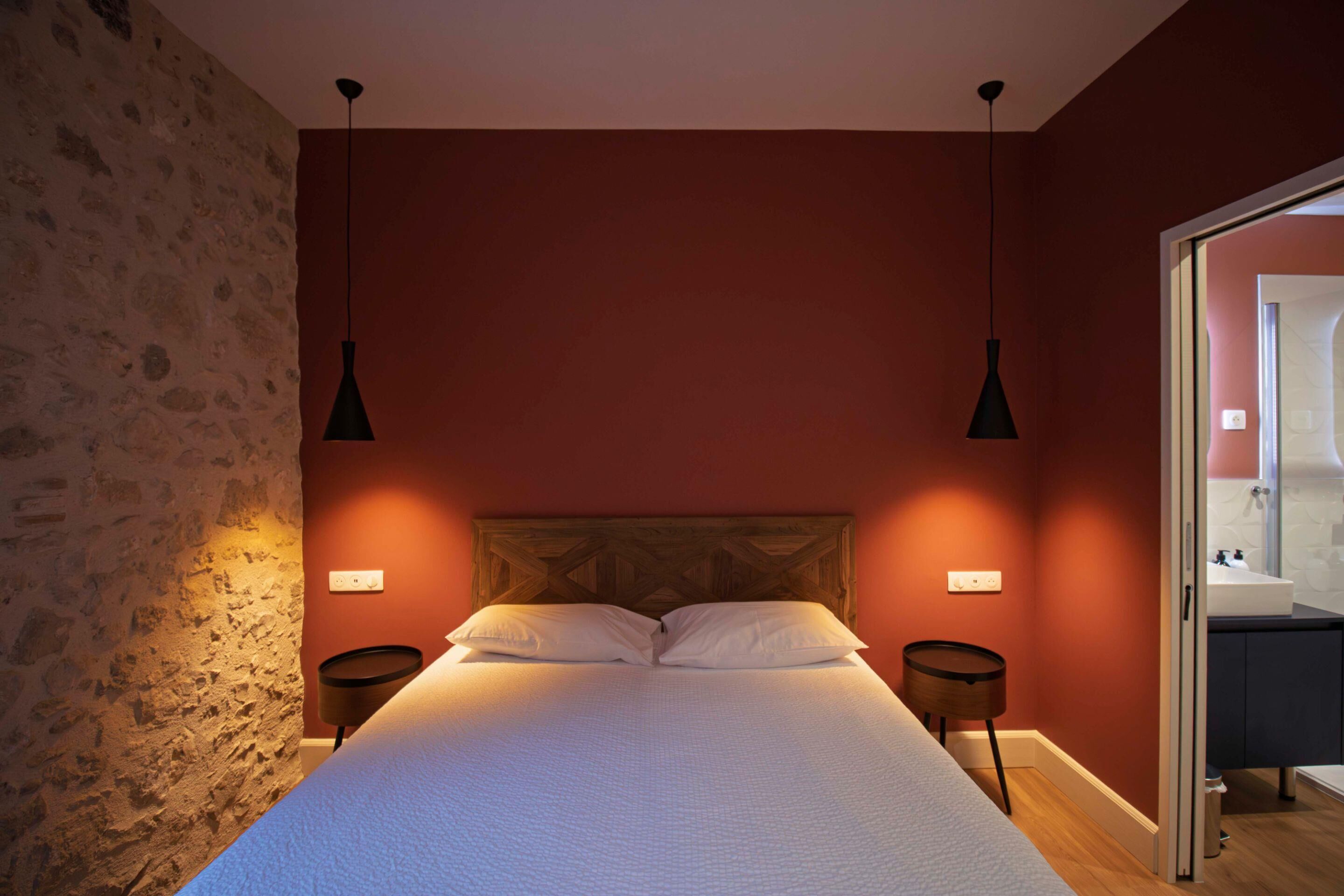 A bedroom with a large bed, two bedside tables, a stone wall, and a wooden headboard.