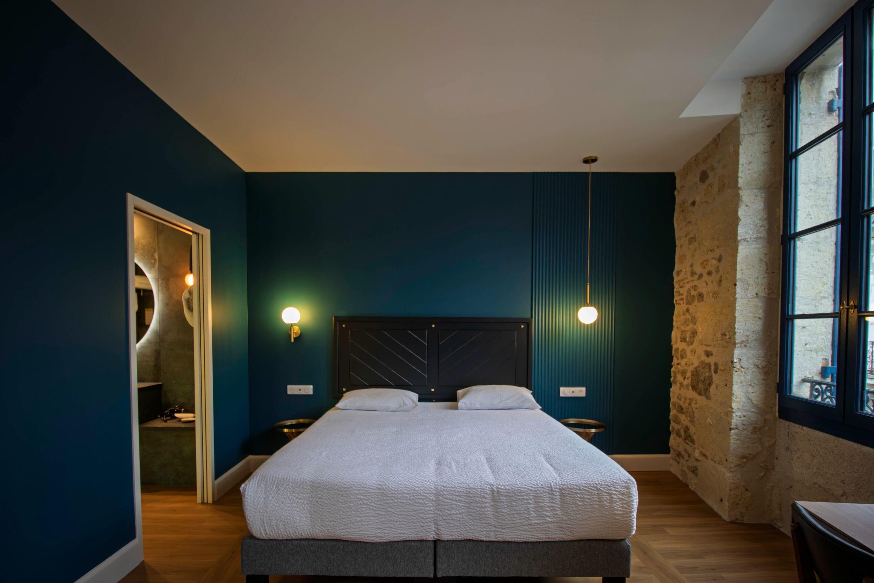 Un dormitorio con una cama, dos mesitas de noche, una ventana y una puerta.
