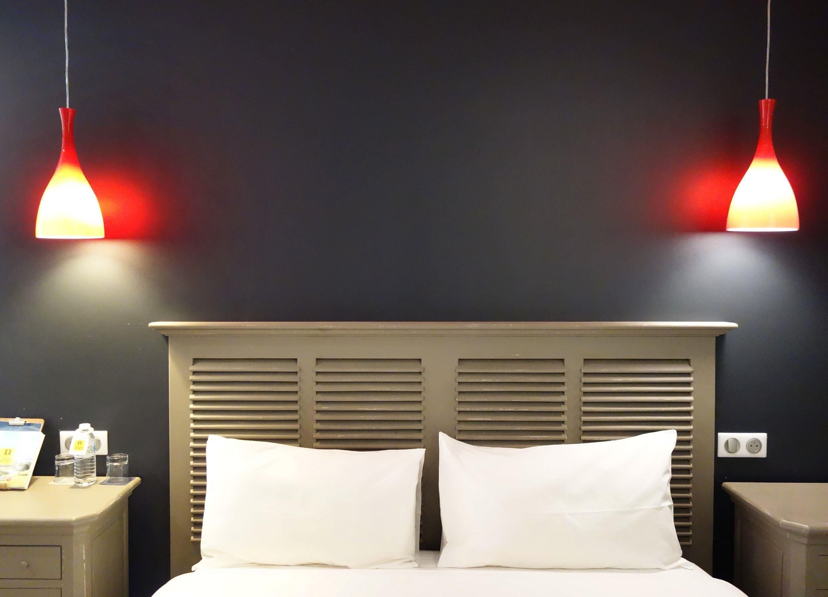 A hotel room with a bed, two bedside tables, and two pendant lights.