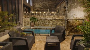 Un patio con mobiliario de mimbre, un muro de piedra, una piscina pequeña y una planta en maceta.