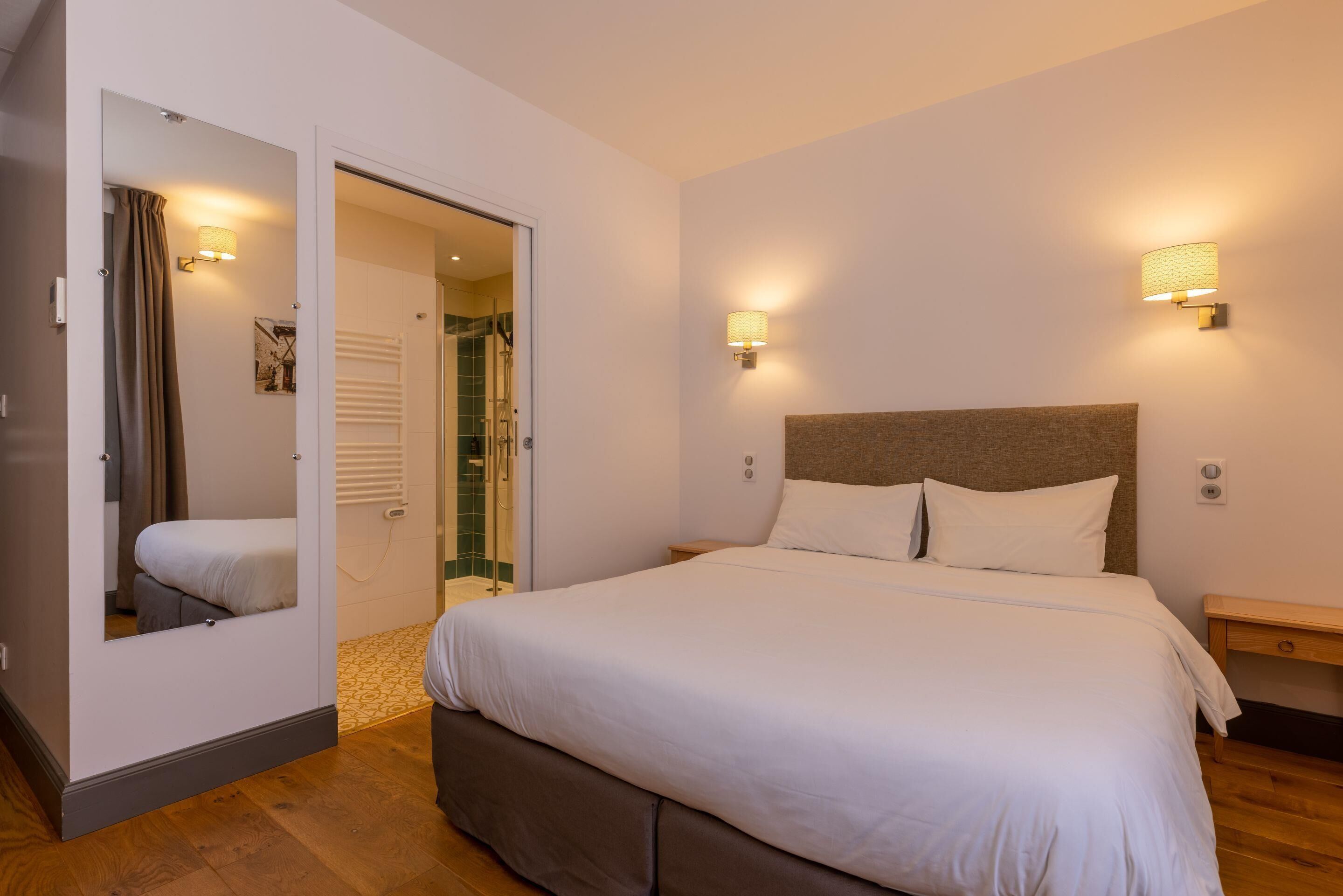 Ein Schlafzimmer mit einem großen Bett, einem Spiegel, einem Nachttisch und einer Wandlampe.