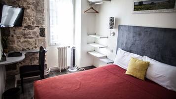 Quarto com parede de pedra, cama com roupa de cama vermelha e branca, televisão, radiador e janela com cortinas.