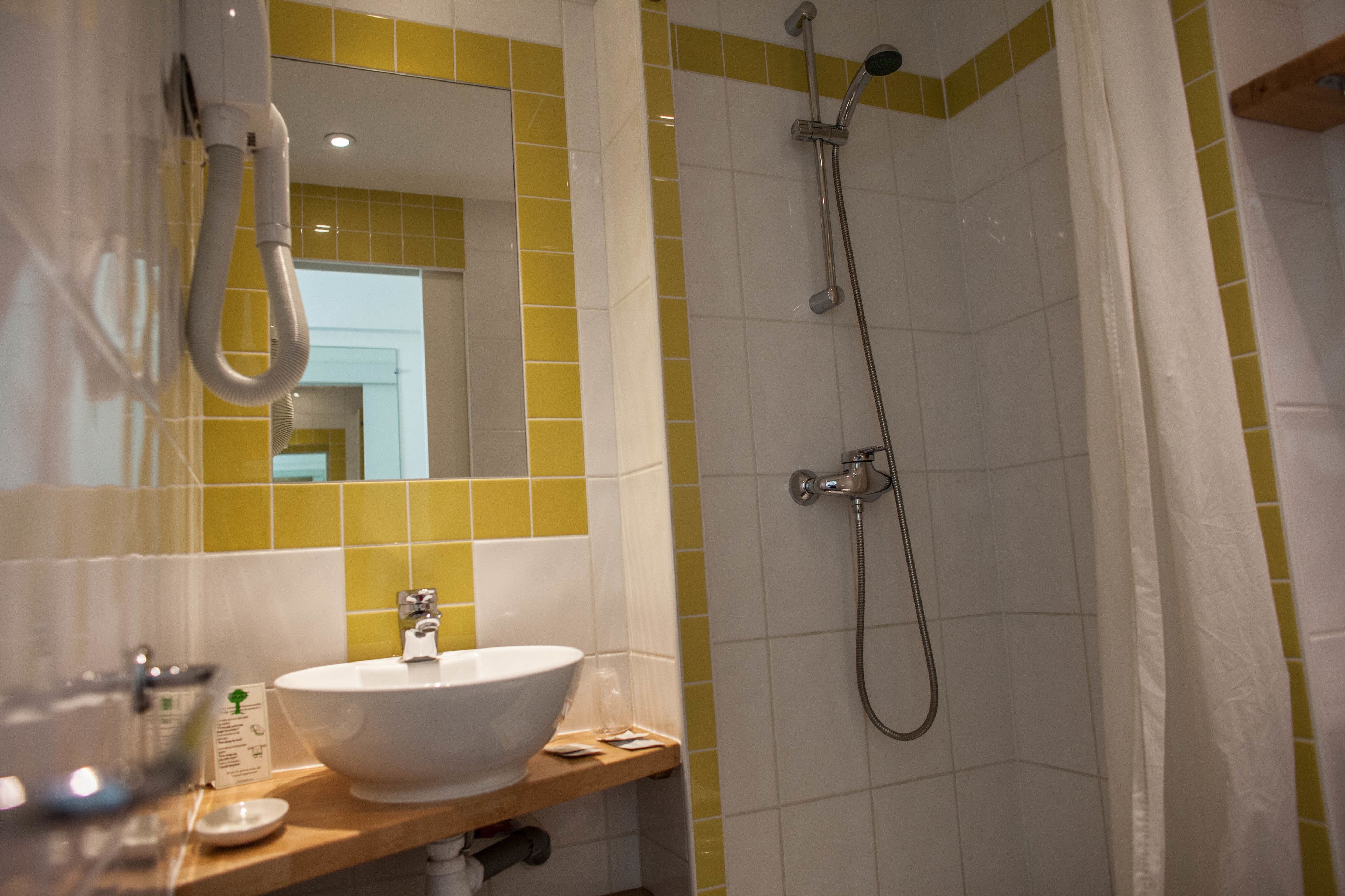 Een badkamer met een wit wastafel, geel betegelde wanden en een douche met gordijn.
