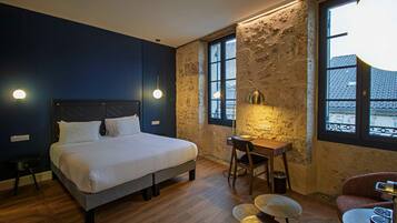 A bedroom with a bed, desk, chair, and a view of buildings through the window.
