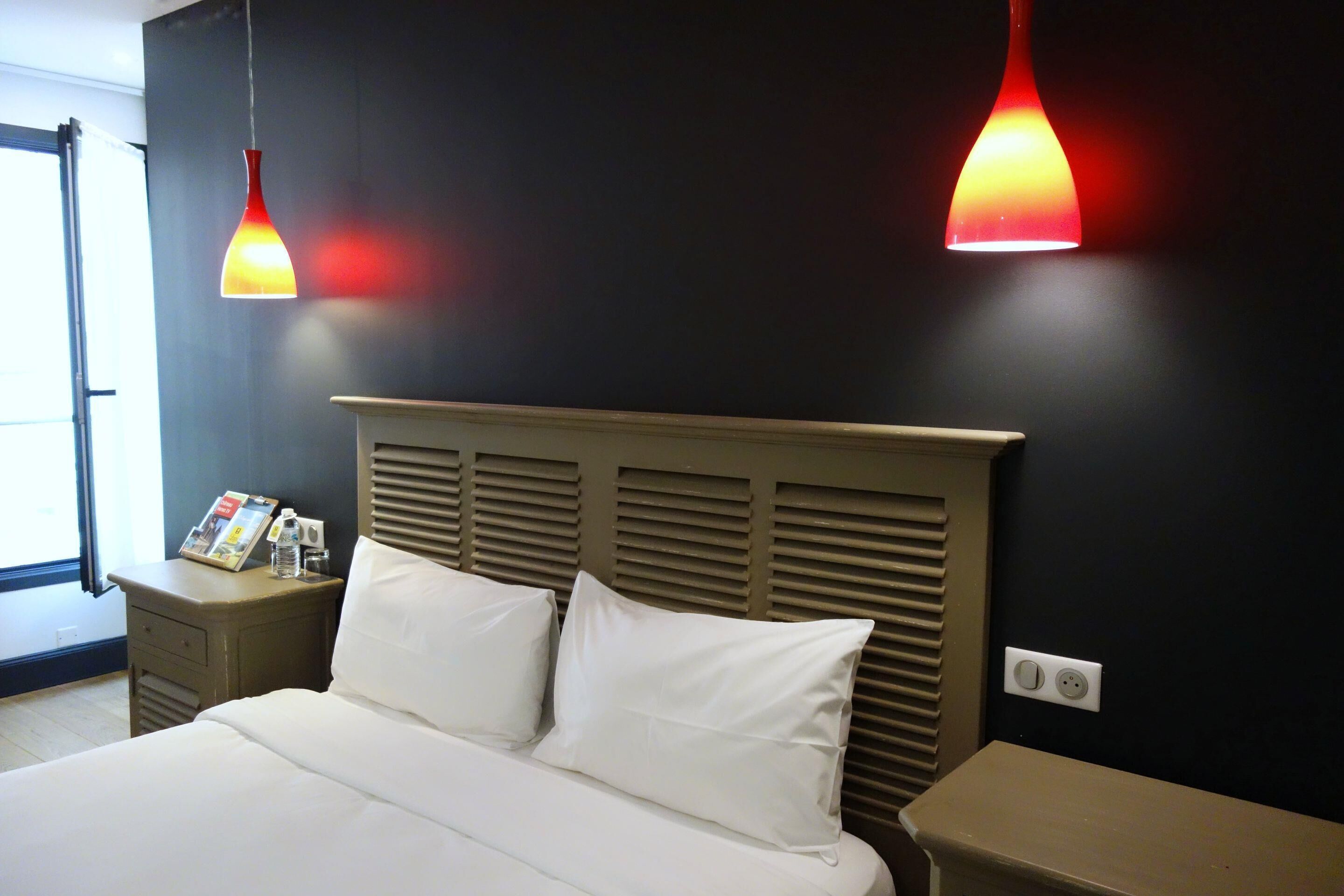 Una habitación de hotel con una cama, mesitas de noche, una revista y dos lámparas colgantes.