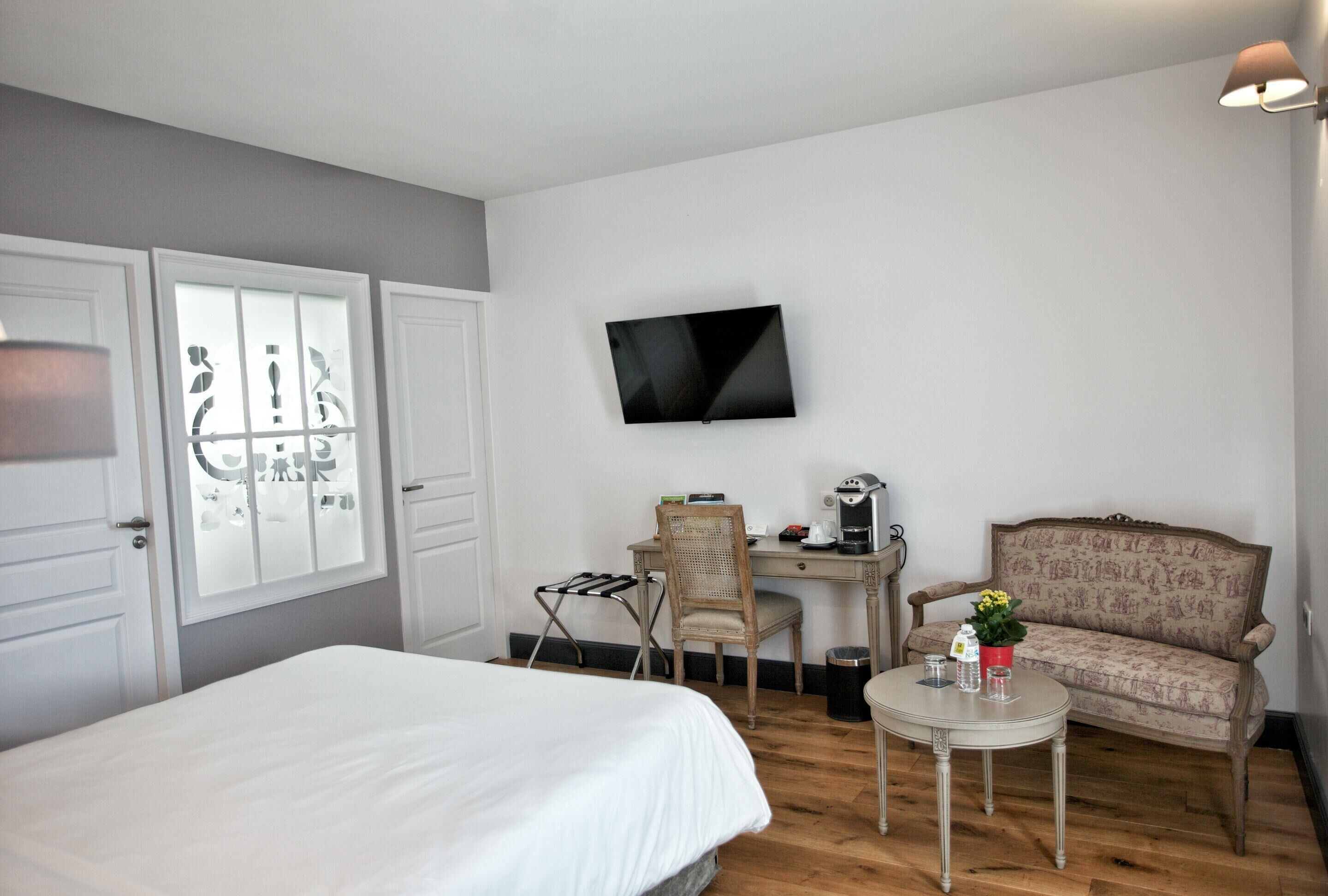 Une chambre d’hôtel comprenant un lit, un bureau avec une chaise, une télévision, une petite table avec une plante et un canapé.