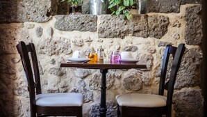Pared de piedra con una mesa preparada para dos personas, que incluye una vela, un vaso y una pequeña planta.
