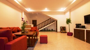 A modern living room with a staircase, red furniture, a flat-screen TV, and a potted plant. - Eco Villa (Siem Reap)