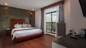A hotel room with a large bed, a desk with a chair, a TV, and a balcony with a view. - Eco Villa (Siem Reap)