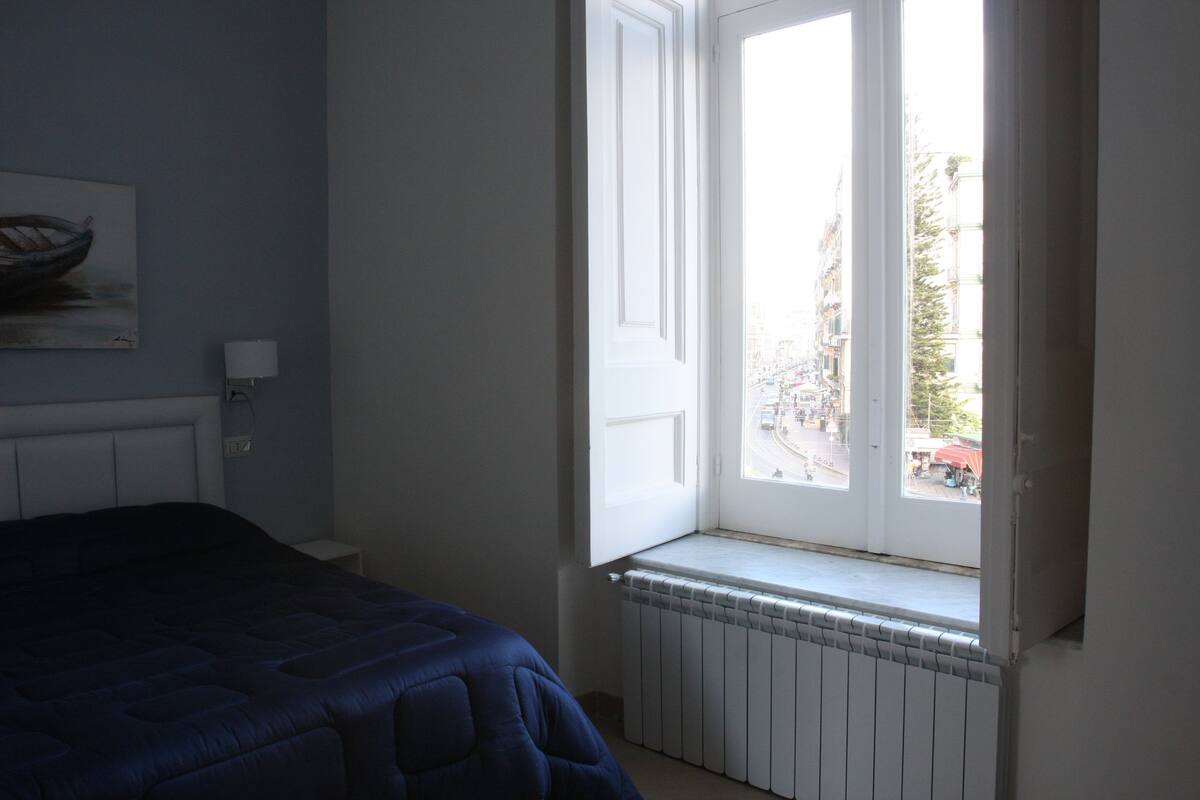 Un dormitorio con cama, un radiador y una ventana que da a la calle.
