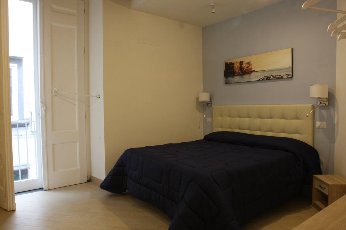 Un dormitorio con cama, una puerta, una lámpara de pared y un cuadro.