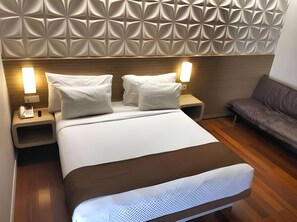 Ein modernes Hotelzimmer mit einem großen Bett, zwei Nachttischen mit Lampen, einem Holz-Kopfteil und einem braunen Ledersofa.