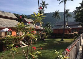 Un hotel de estilo bungalow con techo de paja, rodeado de exuberante vegetación y palmeras.