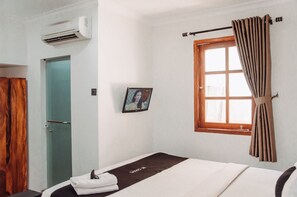 A hotel room with a bed, a window with curtains, a picture on the wall, and an air conditioning unit. - DS Residence Sinabung (Semarang)