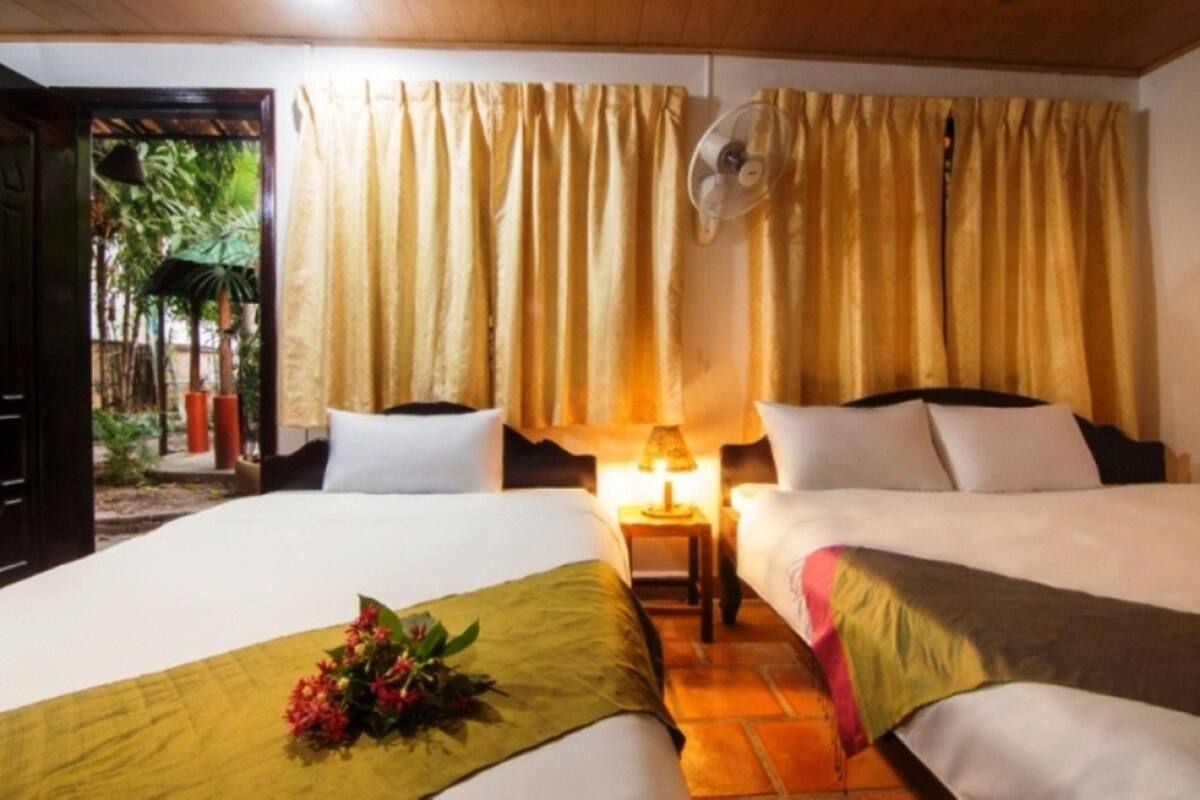 Una habitación de hotel con dos camas, una mesita de noche con lámpara y cortinas.