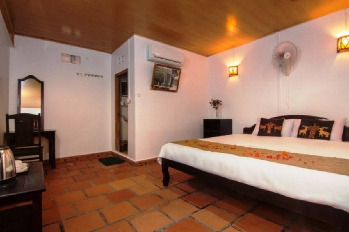 Un dormitorio con cama, mesita de noche, espejo, unidad de aire acondicionado y ventilador de pared.