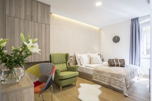 A modern bedroom with a green armchair, a bed with patterned bedding, a clock on the wall, and a window with curtains. - Centro di Centri Rooms (Split)