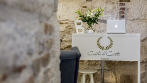 Una habitación con pared de piedra, un escritorio blanco con una computadora portátil, un jarrón con flores y un cartel que dice "Centro di Centro ROOMS".