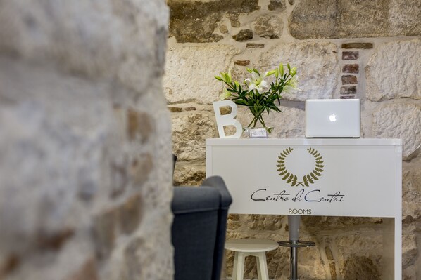 A room with a stone wall, a white desk with a laptop, a vase with flowers, and a sign reading "Centro di Centro ROOMS". - Centro di Centri Rooms (Split)
