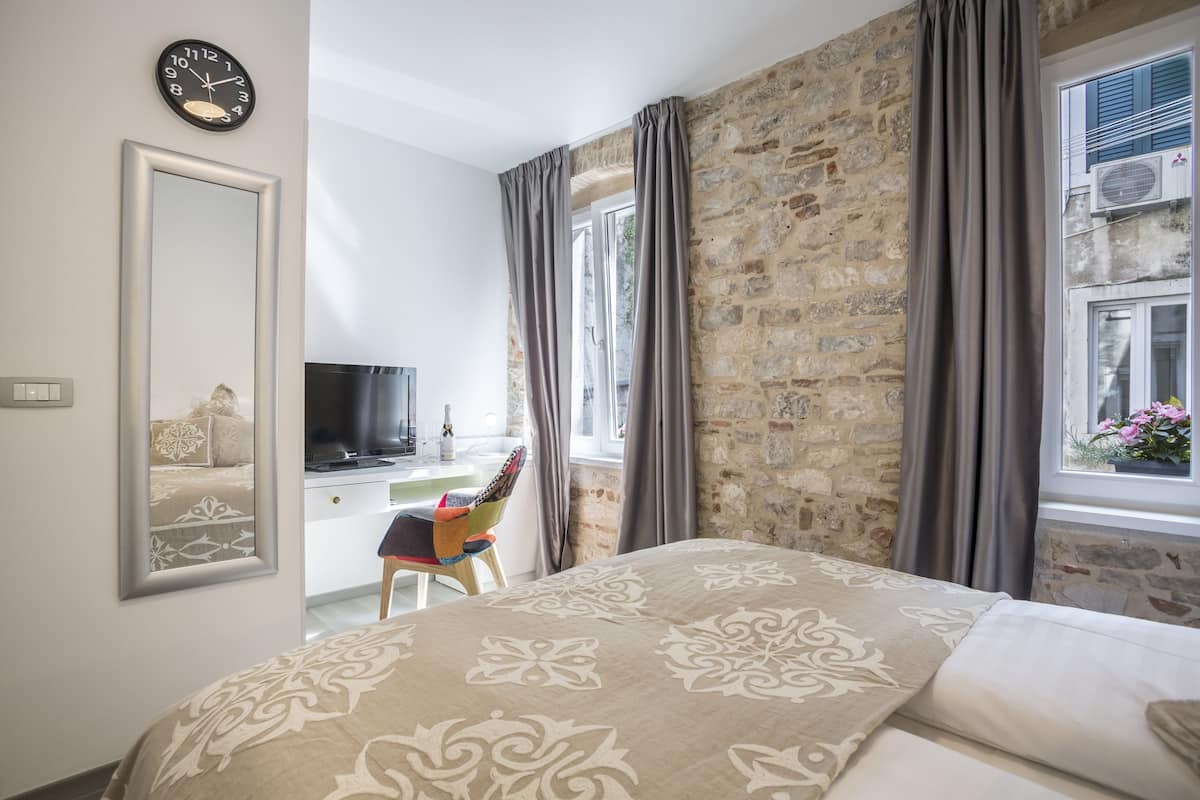 Un dormitorio con cama, escritorio, silla, televisión y ventana con cortinas.