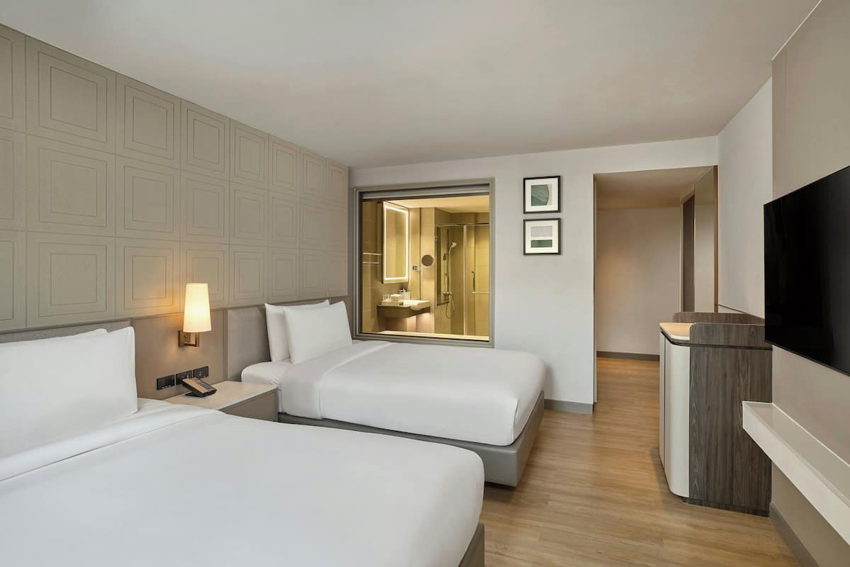 A hotel room with two beds, a TV, a desk, and a bathroom visible through an open door.