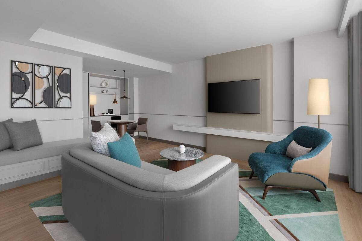 A modern living room with a grey sofa, a blue armchair, a round coffee table, and a flat-screen TV mounted on the wall.