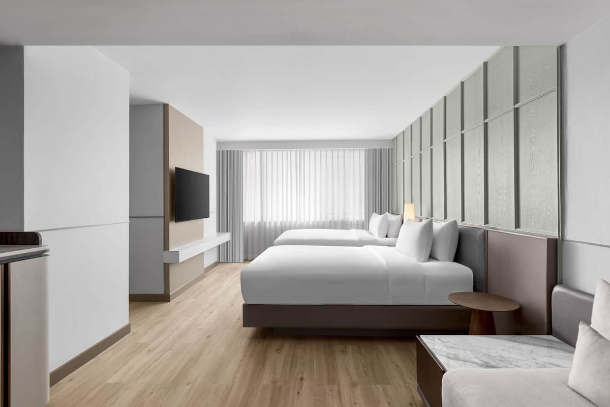 A modern hotel room with a large bed, a TV, a small table, and a seating area.