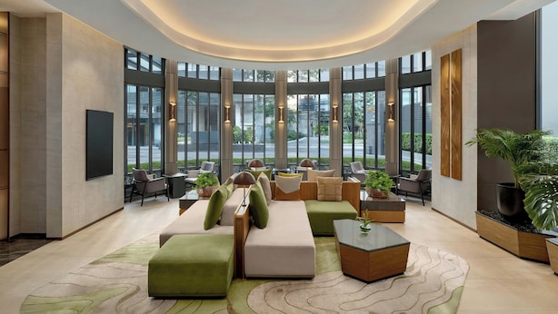 Een moderne lobby met een gebogen plafond, grote ramen en diverse zithoeken, waaronder banken en stoelen.