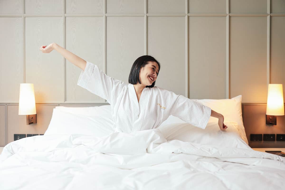 A hotel room with a bed, two bedside lamps, and a headboard with a panel design.