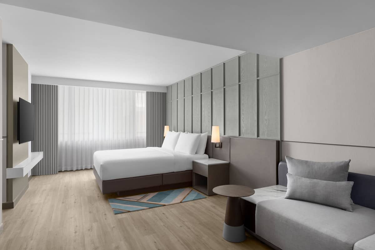 A modern hotel room with a large bed, a sofa, a small table, and a TV mounted on the wall.
