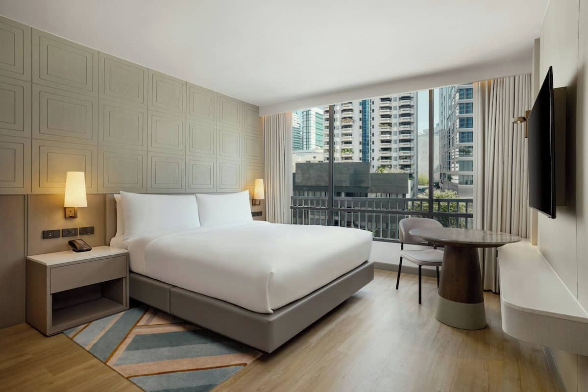 A modern hotel room with a large bed, bedside lamps, a small table, and a TV.