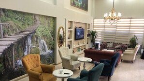 A spacious living area with a large mural of a waterfall, comfortable seating, a television, and a chandelier. - Sanli Hotel (Trabzon)