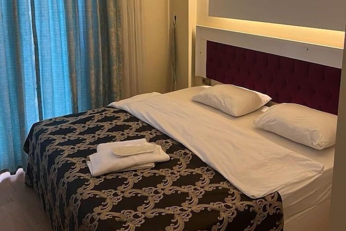 Una habitación de hotel con cama, cortinas y cabecero.