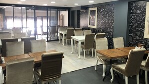 A modern dining area with white tables and chairs, a black patterned wall, and a large window with natural light. - Sanli Hotel (Trabzon)