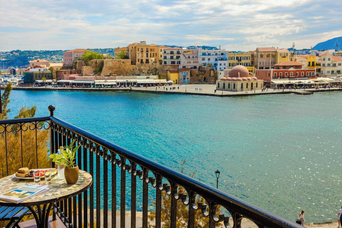 Un pueblo costero con un paseo marítimo, edificios de arquitectura diversa y un área de restauración con mesas al aire libre.