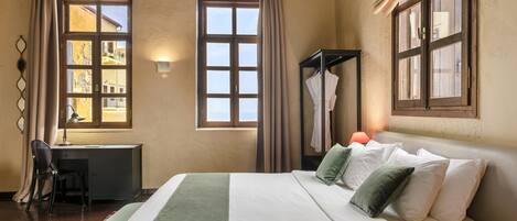 Habitación de hotel con cama, escritorio, silla y dos ventanas con cortinas.