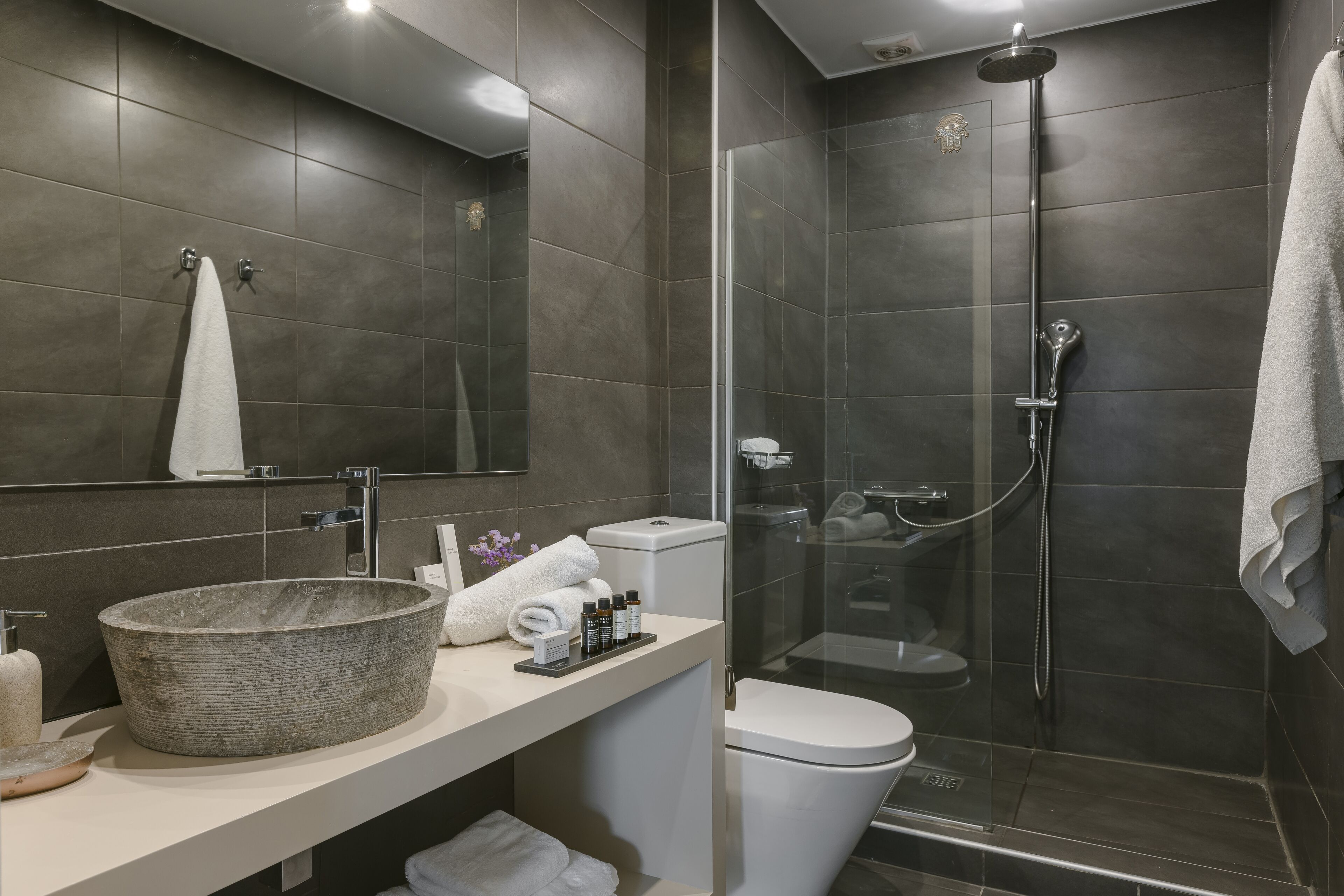 A modern bathroom with a large stone sink, a toilet, and a glass-enclosed shower area.
