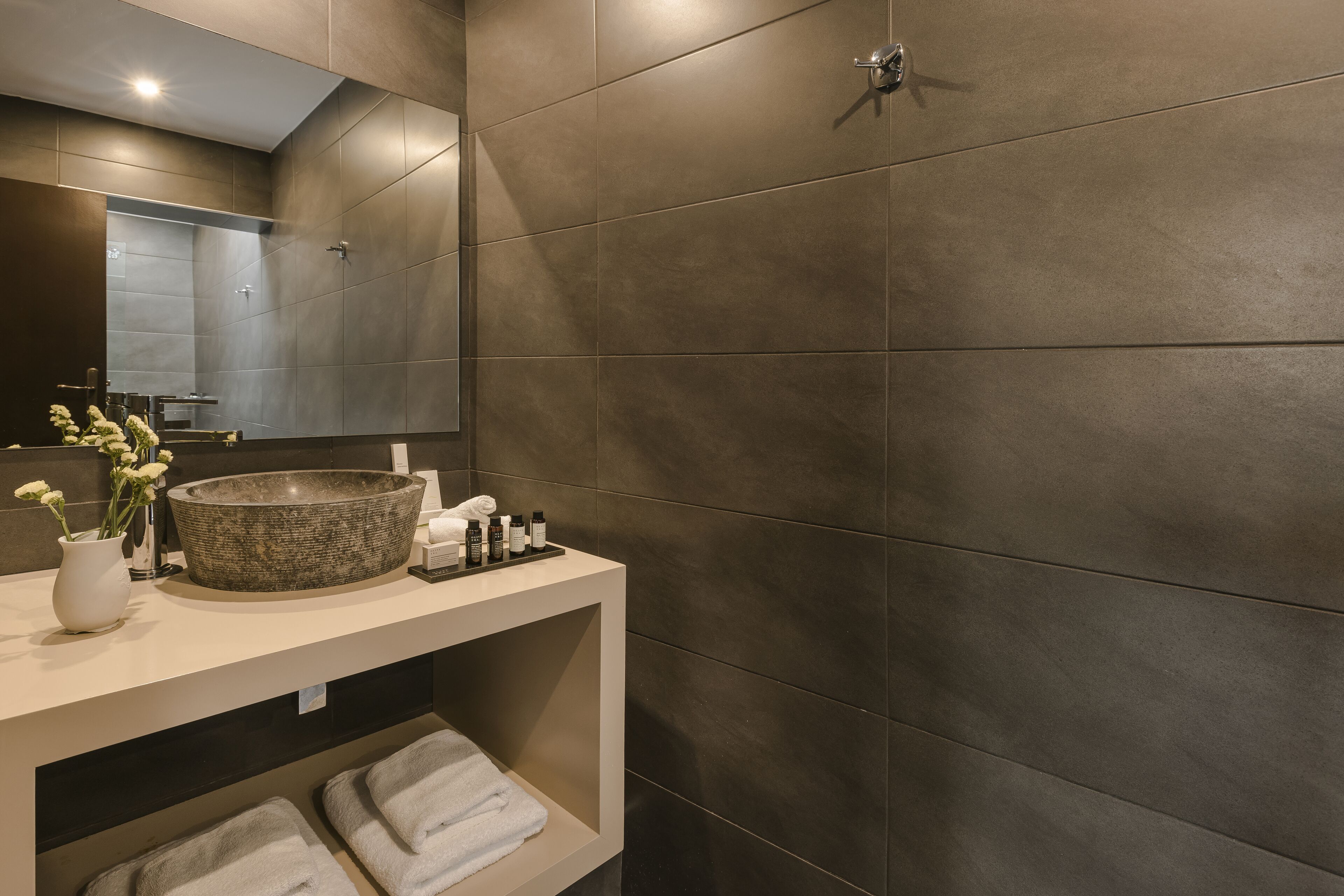 Un baño moderno con un lavabo redondo grande, un espejo y un estante con toallas y artículos de aseo.