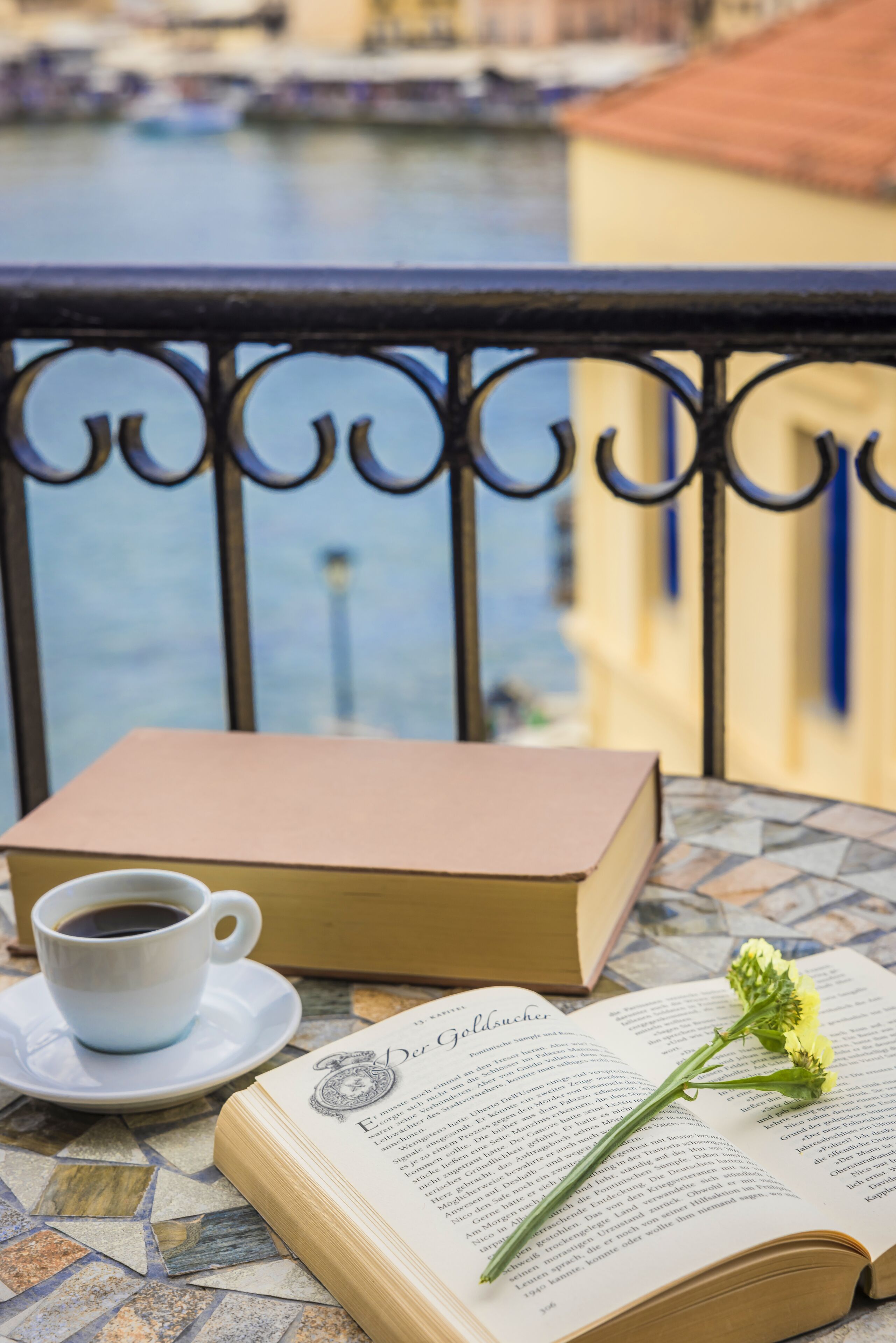 Un libro abierto con una flor encima, una taza de café y un libro sobre una mesa con suelo de baldosas.