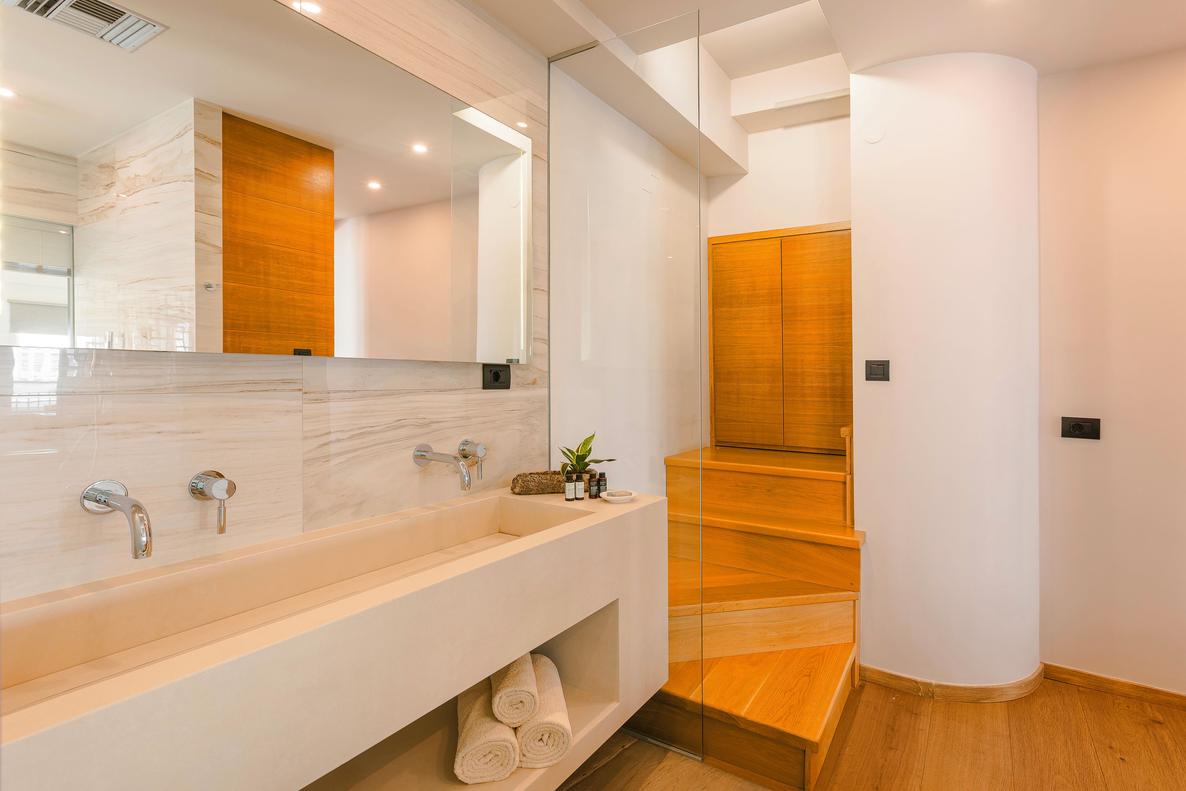 A modern bathroom with a marble sink, wooden accents, and a glass shower enclosure.
